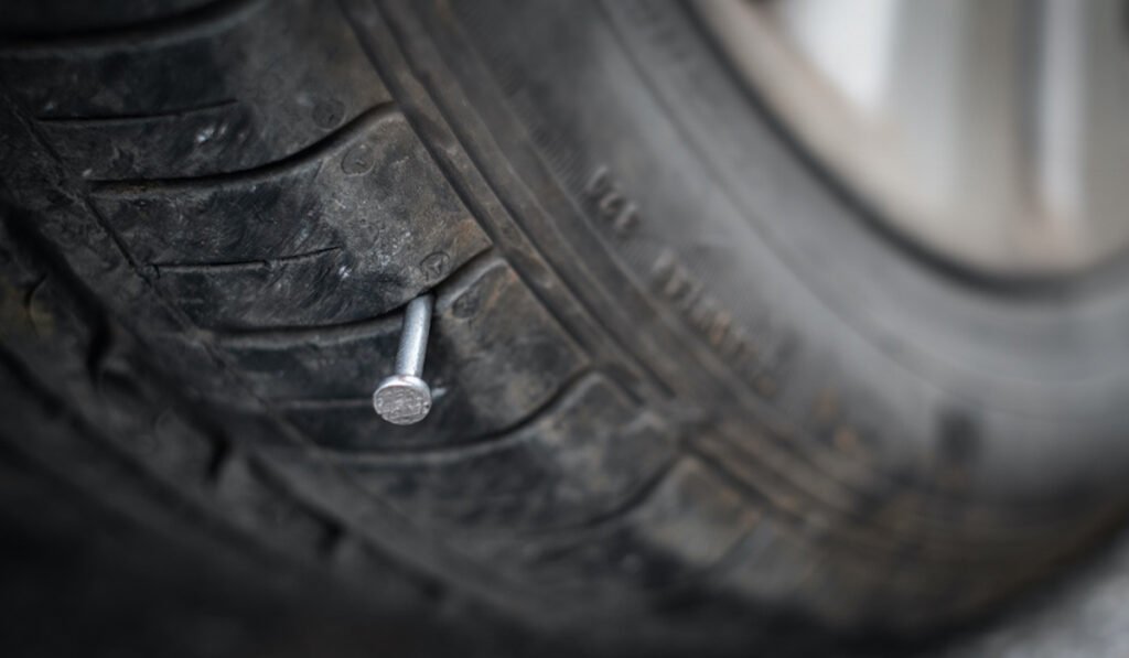 alt="Close-up of a tire punctured by a nail causing air leakage